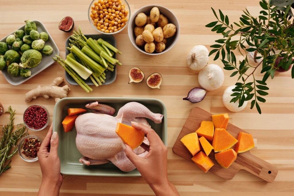 Hands preparing chicken with fresh vegetables on a wooden table.